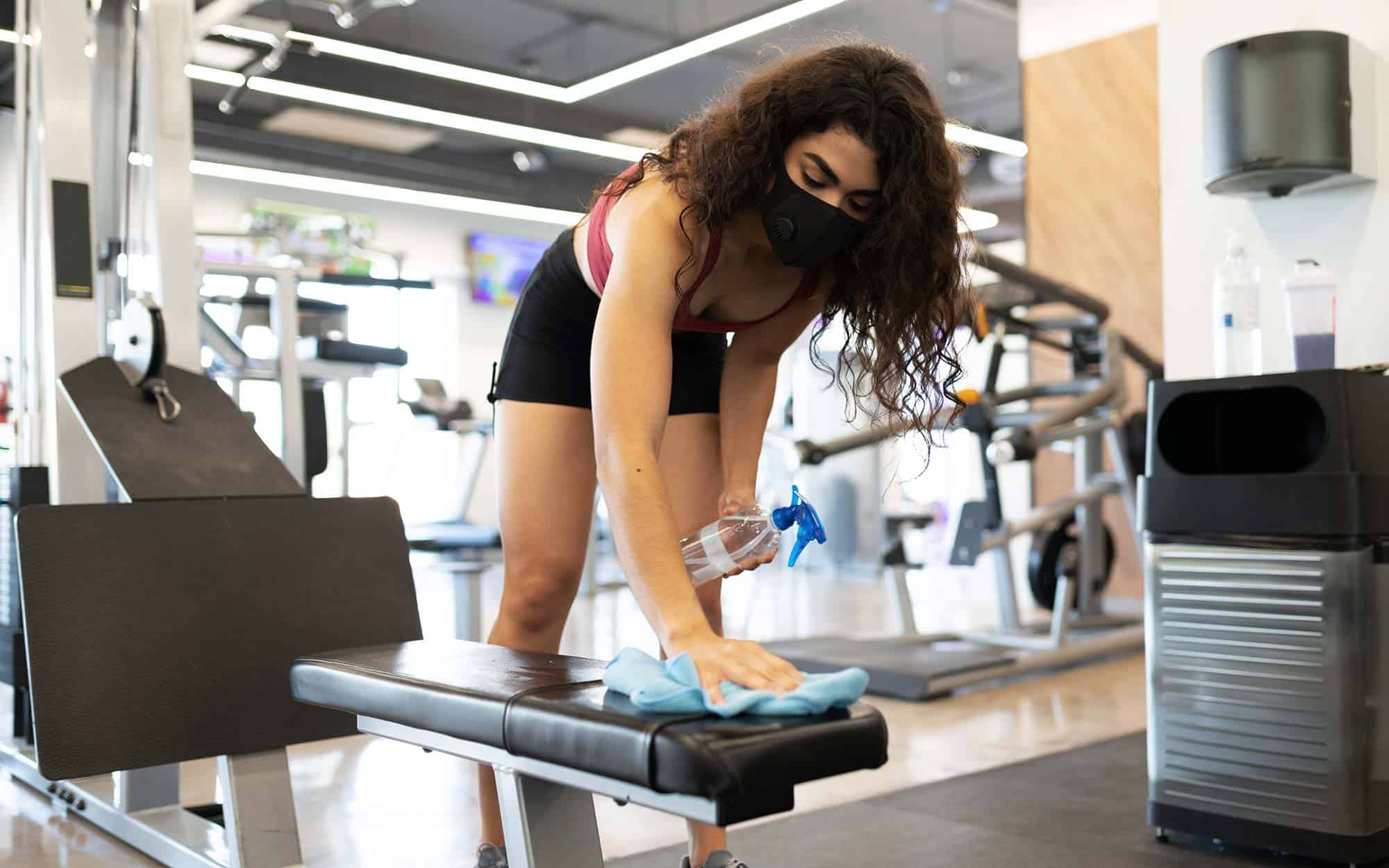 Hispanic woman desinfecting the gym equipment