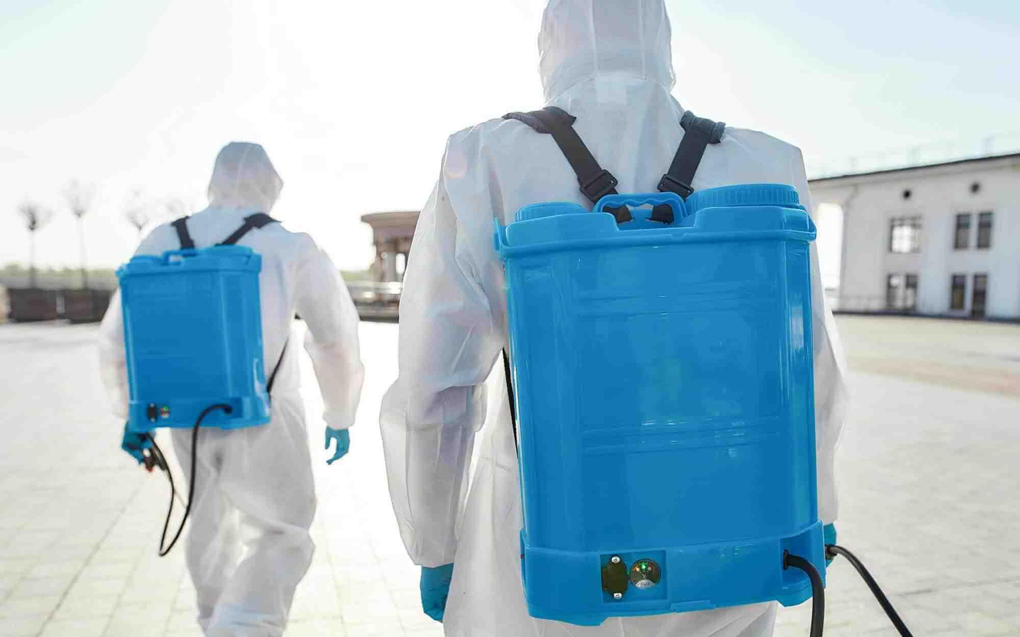 Specialized team in protective suits and masks with backpack of pressurized spray disinfectant